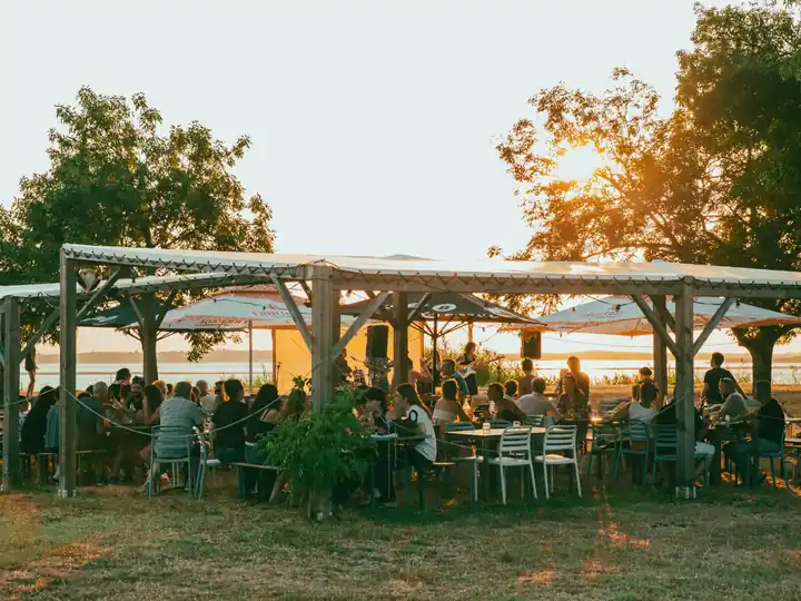 La Guinguette du Peyrat au coucher du soleil, convives attablés sous la pergola au bord de la Gironde