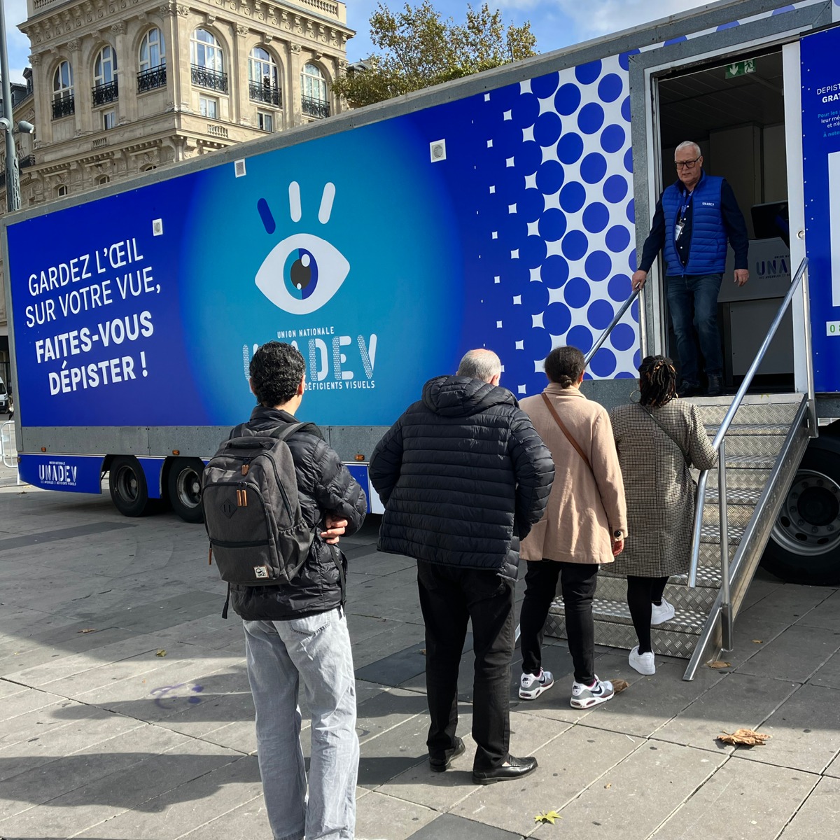 Unité mobile de dépistage visuel UNADEV déployée sur une place publique à Lyon, avec file d'attente de citoyen·ne·s. - réalisé par Agence Kulte